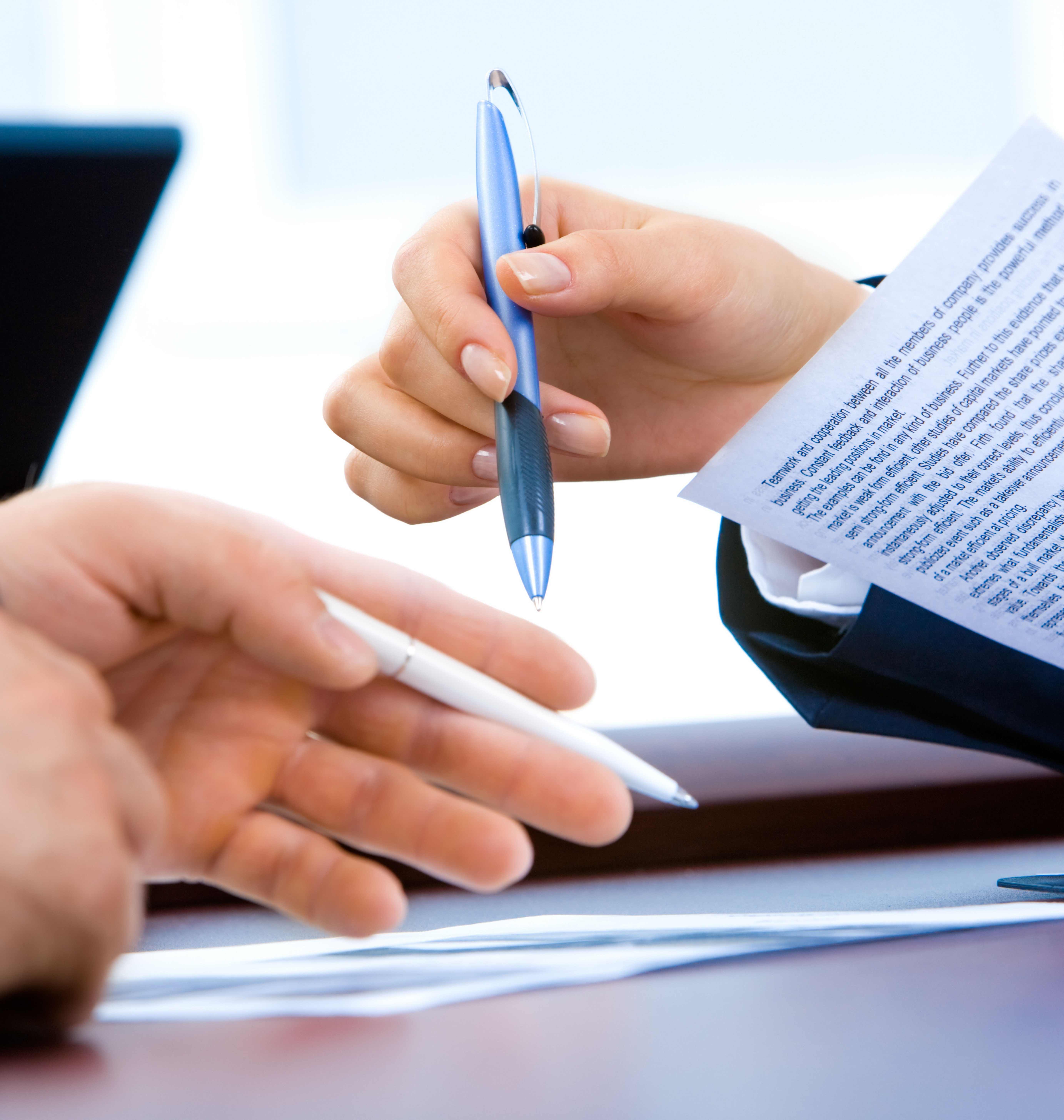 One male and one female hand holding pens and paper, in a business scene